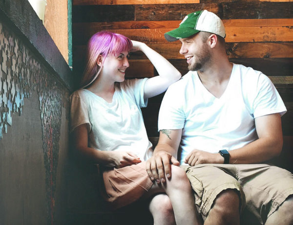 A woman looking at the man she’s interested in wondering, “Is he flirting with me?” while he touches her knee as they talk in a bar.