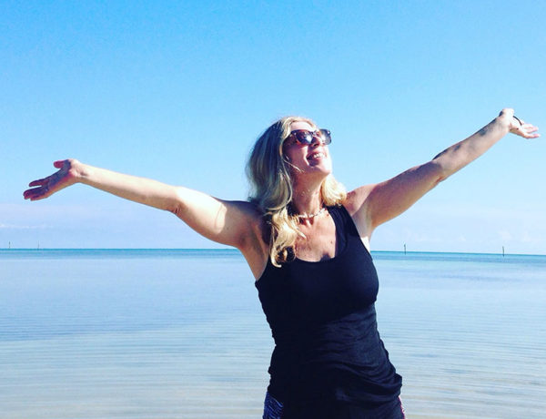 A woman who listened to these breakup tips at the beach with her arms out, embracing life because she’s getting over it.