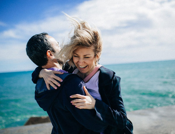 A couple that learned these ways to show love and affection laughing and hugging on the beach.