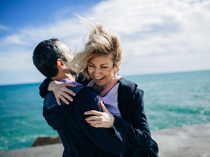 A couple that learned these ways to show love and affection laughing and hugging on the beach.