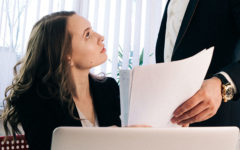 A woman looking for signs your married coworker is fliriting, looking at her coworker as he hands her a paper.