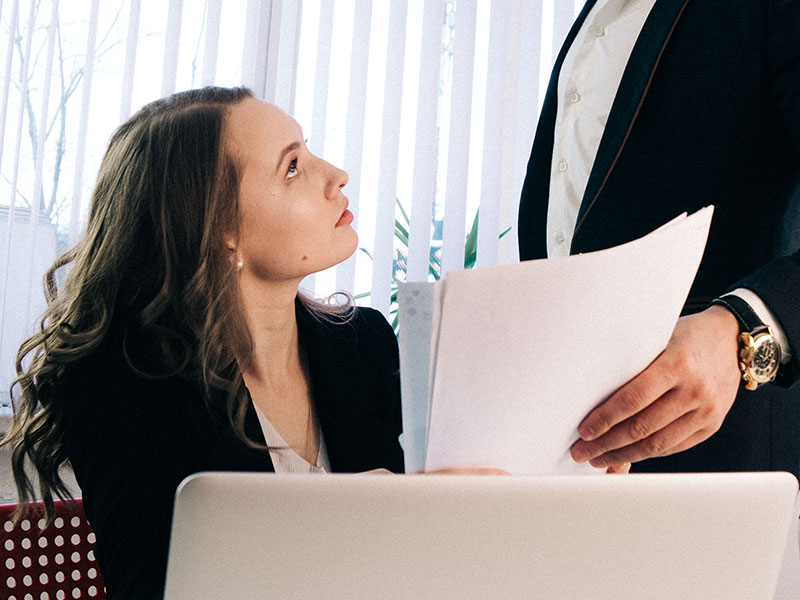 A woman looking for signs your married coworker is fliriting, looking at her coworker as he hands her a paper.