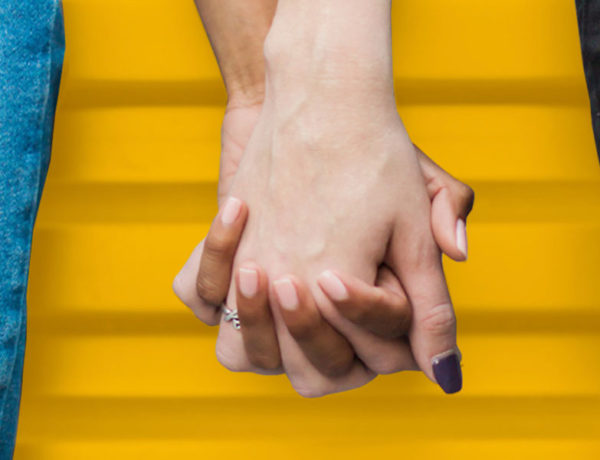 Two women who learned what is Bumble, holding hands in front of a house the distinctive yellow color of the app.