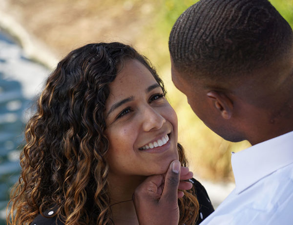 A single woman smiling as her date holds her chin on the beach.