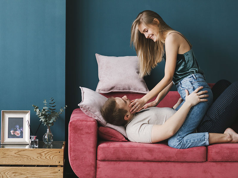 A woman who learned how to seduce a man, straddling her boyfriend on a couch, preparing to kiss him.