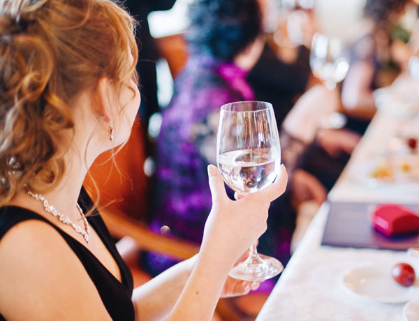 A guest at a wedding holding her glass of water looking around the room for someone to flirt with.