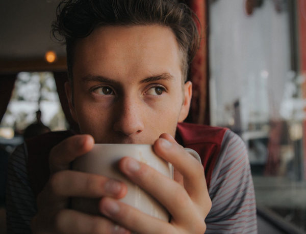 A guy drinking coffee and wondering, “Should I break up with my girlfriend?” while looking out the window.