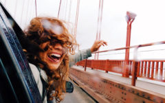 A woman who's letting go of someone, hanging out a car door window with a smile as she goes over a bridge and moves on with her life.