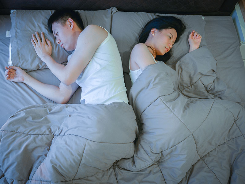 A couple in an unhappy relationship in bed together, facing opposite directions.