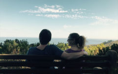 A couple who's out of the honeymoon phase relaxed and comfortable on at bench after a hike.