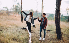 A girl who's wondering "is he thinking about me?" balancing on a log while the guy she likes helps her and looks on with a smile.