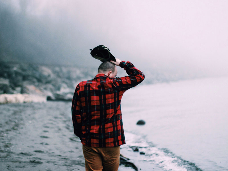 An emotionally unavailable man walking down a foggy beach and thinking.