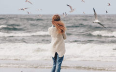 A woman who's wondering why her boyfriend is acting weird, standing on the beach alone and wondering.