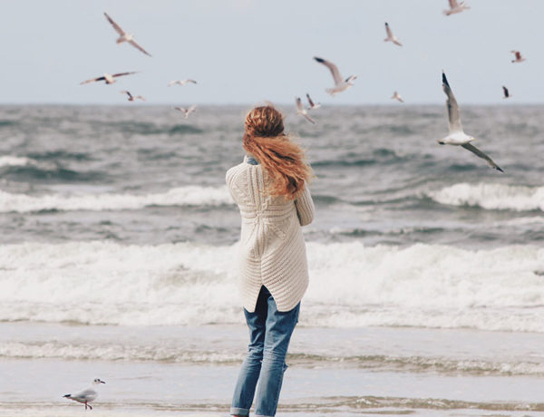 A woman who's wondering why her boyfriend is acting weird, standing on the beach alone and wondering.