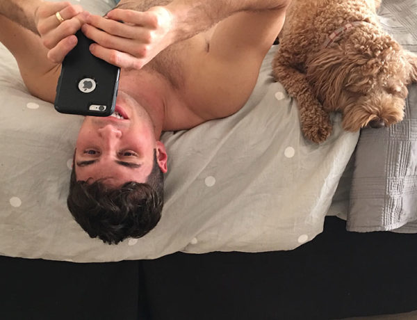 A guy writing Tinder messages while in bed with his dog next to him.