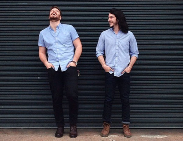 Two men who are life partners standing against a wall and laughing together in their engagement photos.