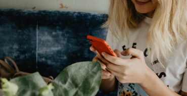A girl responding to a Tinder first message and laughing on her couch at home.