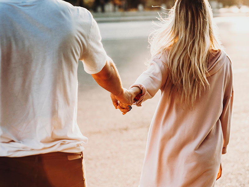 A woman dating an older man, leading him through the street as she holds his hand smiling and flirting.