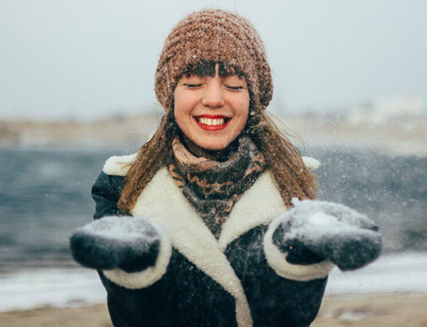 A woman who's learned how to stop attracting players, smiling as she plays in the snow and let's it fall on her.