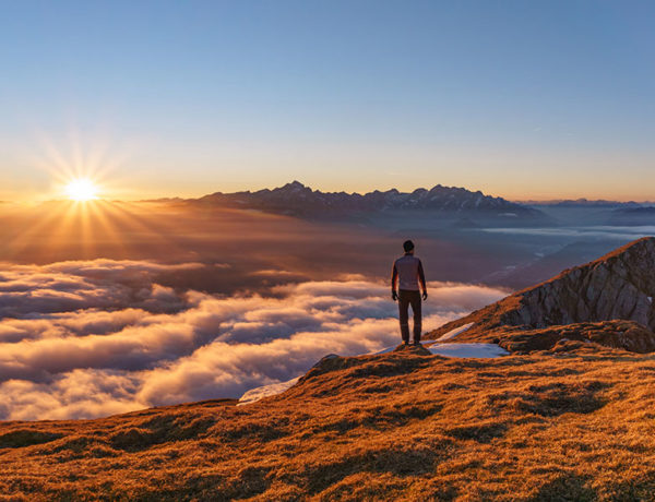 A guy who learned what to do after a breakup, standing on top of a mountain he just climbed up looking proud and reflective.