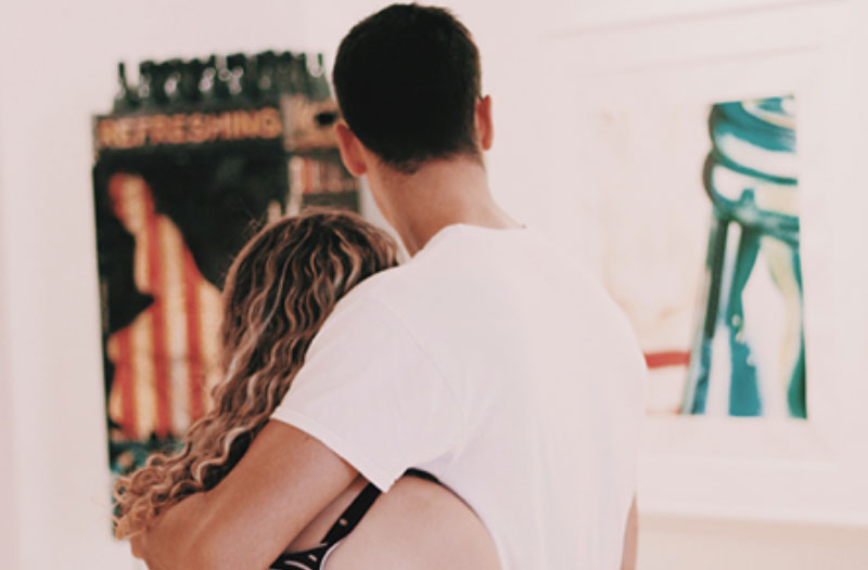 A couple hugging in front of a painting while on a winter date idea at a museum.