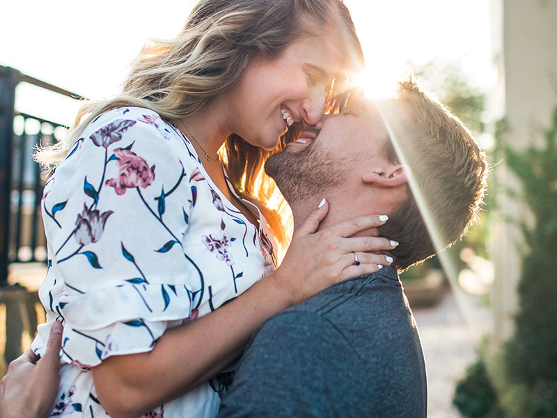 A woman who learned how to make him want you, about to kiss a buy outside in the sun.