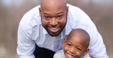 A dad who is dating someone with kids, playing with their kid and laughing in a field.