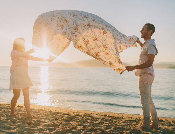 A couple using one of these unique date ideas as they spread out a picnic blanket on the beach.