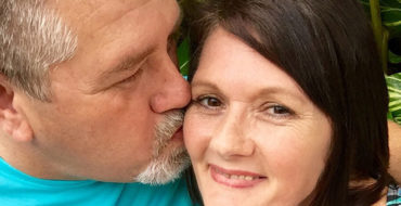 A couple dating after 50 smiling as the man kisses the woman's cheek.