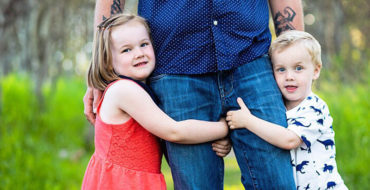 A woman who's dating a man with kids and feeling left out looking at two kids hugging their dads legs.