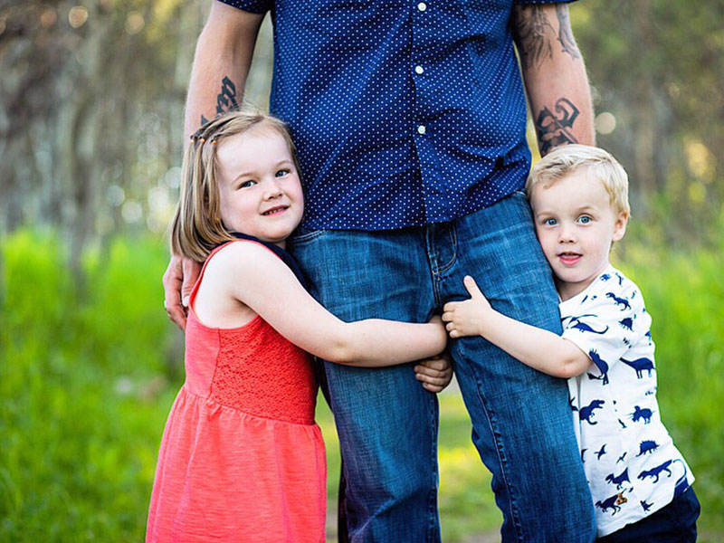 A woman who's dating a man with kids and feeling left out looking at two kids hugging their dads legs.