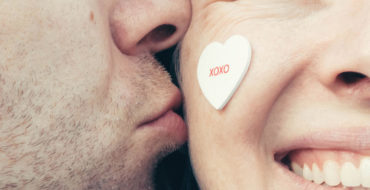 A couple that met on over 50 dating sites, smiling as the man kisses the woman's cheek.
