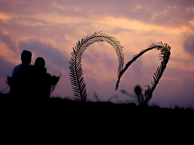 A couple who used one of these Valentine's Day date ideas, sitting on a hill watching the sunset.
