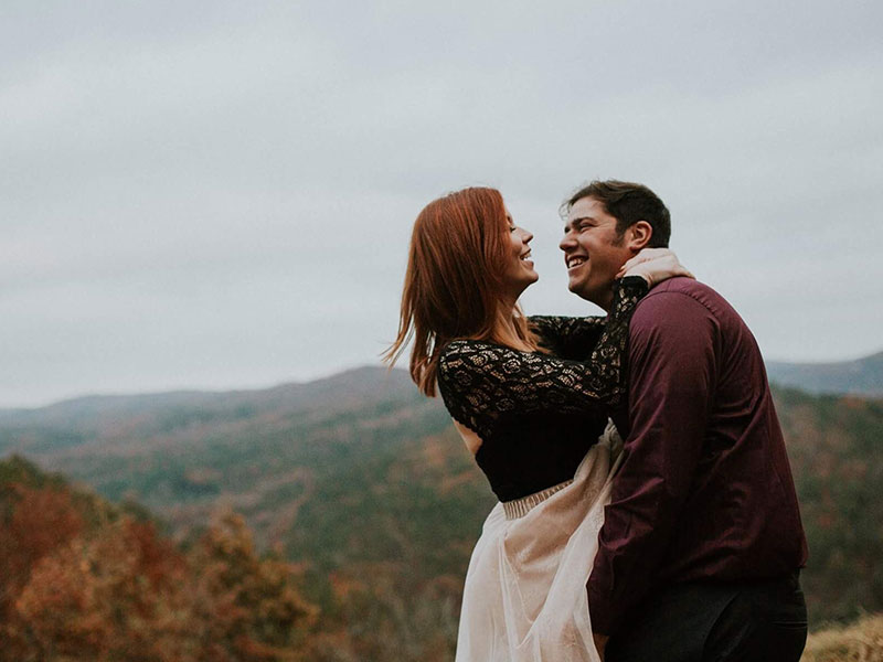 A couple who took these empowered dating tips laughing as they're about to kiss on top of a mountain.