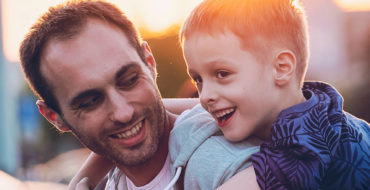 A man dating with kids, laughing with his son on his back.