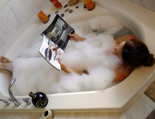 A woman in a bathtub reading a magazine in a bubble bath relaxing.