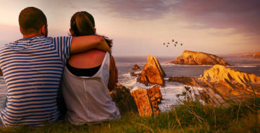 A couple who used on of these first date ideas, sitting on top of a hill looking at the sunset after a hike.