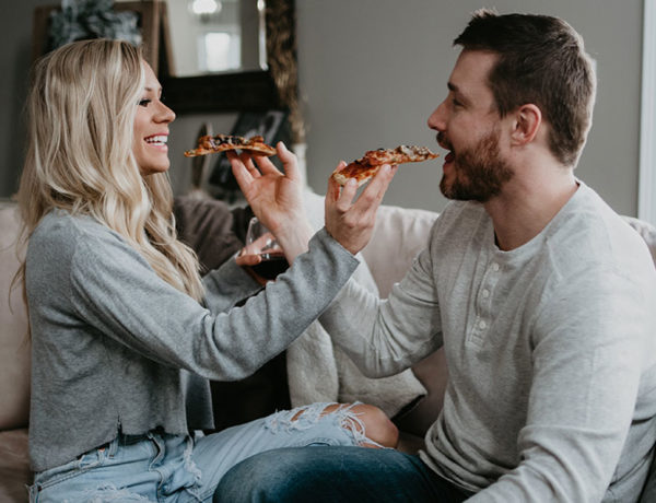 A couple using one of these cheap date night ideas and sharing pizza at home on the couch.