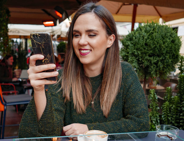 A woman receiving cute texts for her from the guy she likes and smiling while she's drinking coffee.
