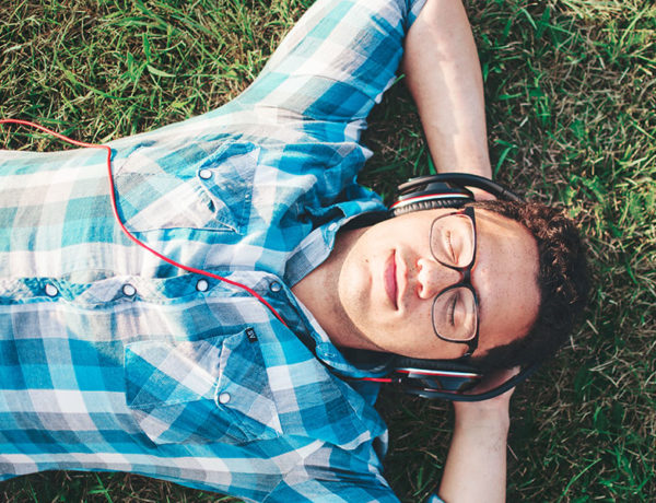 A guy lying in the grass and smiling as he listenings to songs about getting over someone on his headphones.