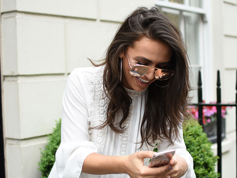 A woman who found some dating sites where messaging is free, texting someone from the app on her phone and laughing outside.