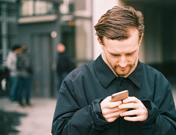 A guy looking through fake Tinder profiles while outside looking confused.