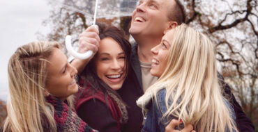 A group of people hugging and laughing under an umbrella showing some of these 3 types of love.