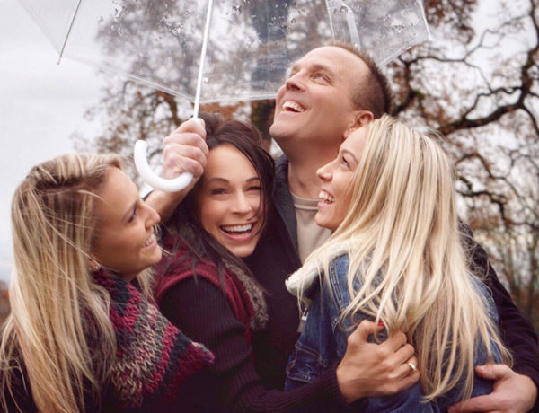 A group of people hugging and laughing under an umbrella showing some of these 3 types of love.