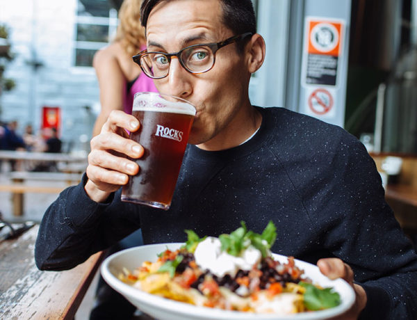 A man at a brewer, drinking a beer and holding some nachos as he takes advantage of one of these good date ideas.
