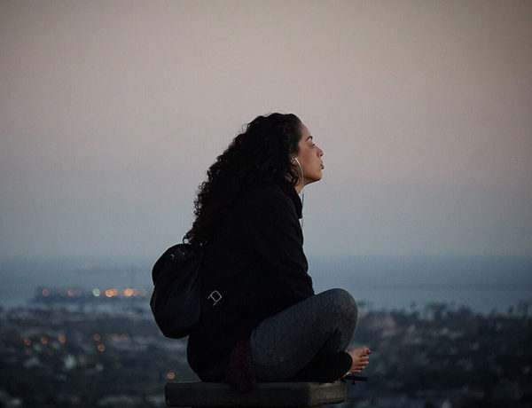 A woman listening to music and songs with these break up lyrics on a hill at sunset as she thinks about where she is.