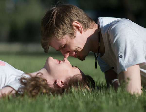 A woman wondering how to attract men, lying in the grass and looking up into the eyes of man flirting with her.