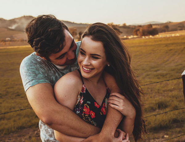 A couple that listened to this love advice, smiling and laughing in a field together as they hug.