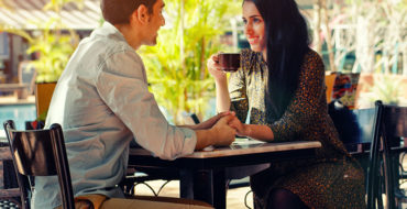 A couple at a table using one of these conversation starters for dating to chat about while they sip coffee.