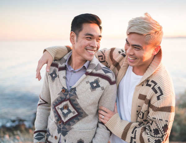 A gay couple on the beach laughing together as they take a photo for social media sites.